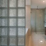 Vidrio block 19x19x8-transparente-oceano-foncer-plomeria garcia-2-ok | Plomería García Modern bathroom with a glass block wall on the left and a glass-enclosed shower on the right, beige tiled floors and walls.